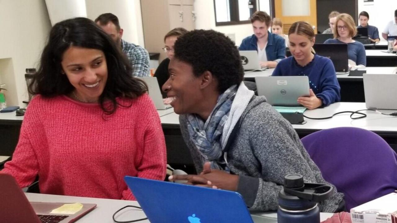 Two students laughing in a classroom with laptops